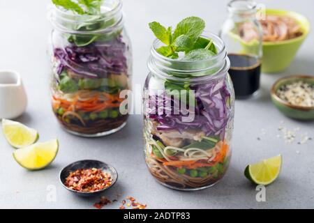 Healthy asian salad with noodles, vegetables, chicken and tofu in glass jars. Grey background Stock Photo