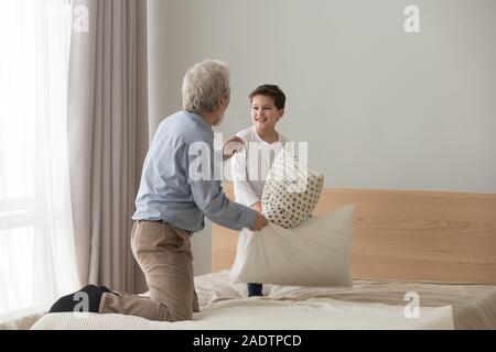 Old grandfather and little grandson fighting holding pillows on bed Stock Photo