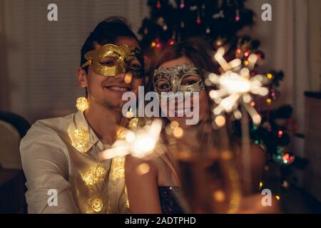 Christmas and New year party concept. Couple in love burning sparklers by illuminated Christmas tree with champagne. Stock Photo