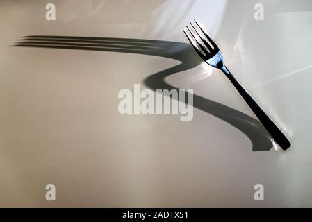 Fork throws large elongate Shadow on glass table background. Concept of Shadow and Light Stock Photo