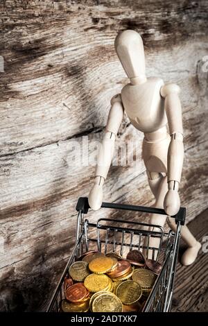 wooden mannequin with shopping cart with coins Stock Photo