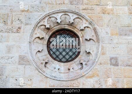 Round window with a black metal fence and a pattern in an old brick and stone facade Stock Photo