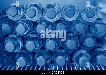 Rows of many transparent plastic bottles with drinking water supply in white refrigerator. Mineral water stack storage in fridge to drink summer day Stock Photo