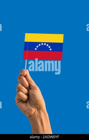 Woman hand holding Venezuela flag with stick, waving flag on deep blue sky. National theme, deep blue sky. Stock Photo