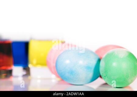 four colorful dyed easter eggs and egg dyes glasses, isolated on white Stock Photo