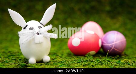 header, funny easter bunny figure and colorful dyed eggs on green moos Stock Photo