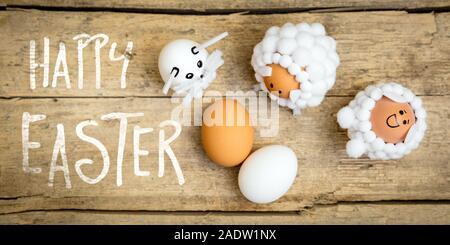 lambs, bunny and eggs on wooden table, english text happy easter, flatlay greeting card Stock Photo