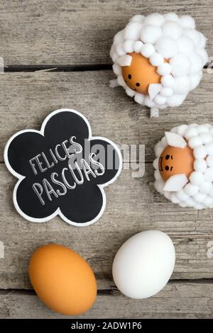 Greeting card with lamb figures and eggs on wooden table, spanish text felices pasquas, which means happy easter Stock Photo