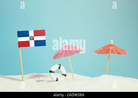 Miniature flag of Dominican Republic on beach with colorful umbrellas and life preserver. Travel concept, summer theme. Stock Photo