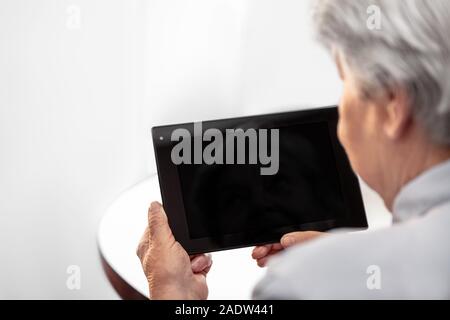Backview of a elderly woman is holding a tablet with copyspace, concept learning and technology Stock Photo