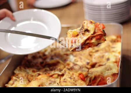 Serving a portion lasagne in a canteen. Lasagne in a tray. White plate. Stock Photo