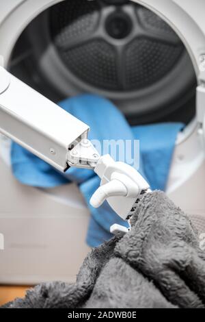ambient assisted living robot or cyborg is working in the household. robot is putting some clothes in the dryer Stock Photo