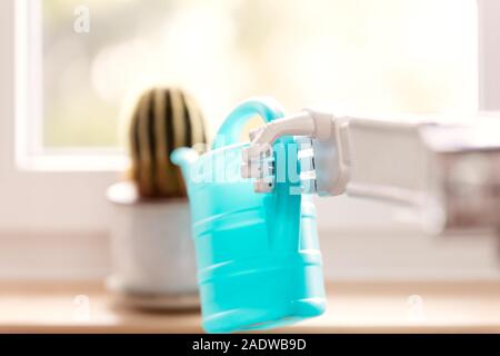 a robotic prosthesis arm with watering can is watering a cactus in front of a window Stock Photo