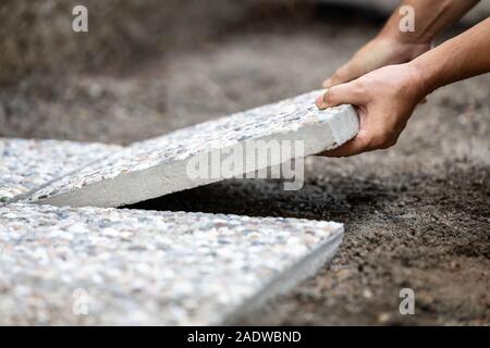 Man moves washed concrete slabs into a gravel bed, freshly laid path out of concrete slabs in the outdoor area Stock Photo