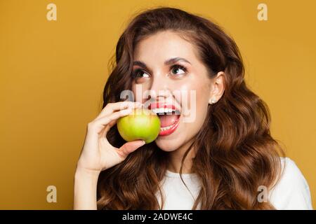 Healthy woman with white teeth biting apple fruit on bright yellow background Stock Photo
