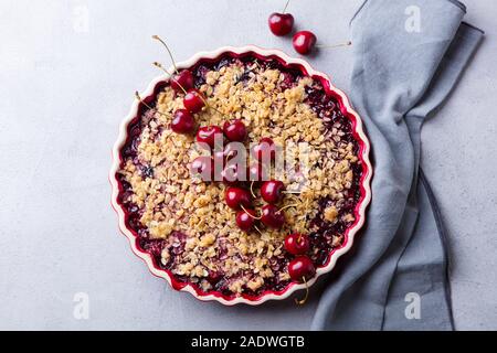 Cherry, red berry crumble in baking dish. Grey stone background. Top view. Stock Photo