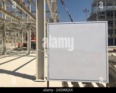 Object under construction stand at the construction site. Blank display board against prefabricated multi-storey building at the background