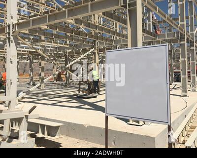 Object under construction stand at the construction site. Blank display board against prefabricated multi-storey building at the background