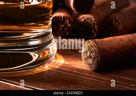 Still life with glass of whiskey or rum, cigar on old wooden board table. Blurred background. Stock Photo