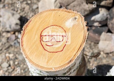 smiling smiley with glasses painted in red. Illustration of smiley emoticon painted on a log. Positive thinking concepts. Stock Photo