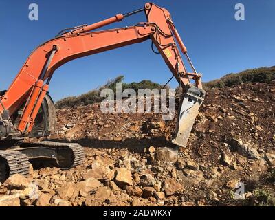 Hydrohammer is crushing rocks during road construction works on the rocky soils. Heavy machinery at earthmoving, digging, excavation operations. Stock Photo