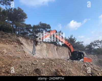 Hydrohammer is crushing rocks during road construction works on the rocky soils. Heavy machinery at earthmoving, digging, excavation operations. Stock Photo