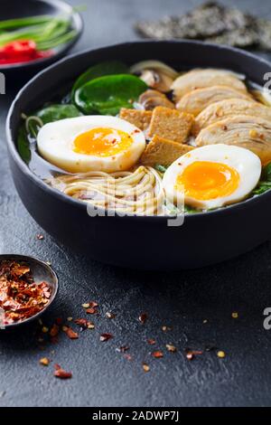 Asian noodle soup, ramen with chicken, tofu, vegetables and egg in bowl. Slate background Stock Photo