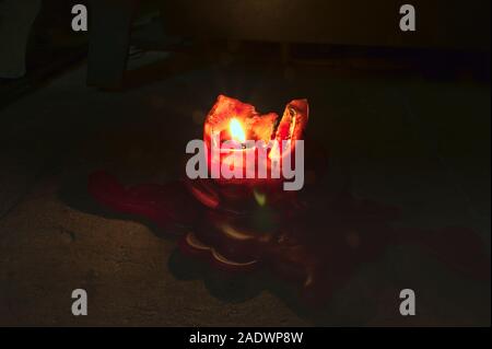 Atmospheric red candle burning in the dark and wax pooling on the floor Stock Photo