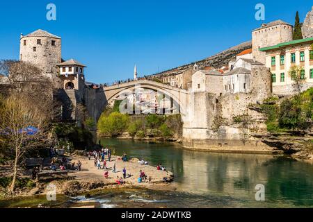 People play and relax along the shore of River Neretva, walk over the rebuilt Stari old bridge in this historic Balkan area,Mostar, Bosnia Herzegovina Stock Photo