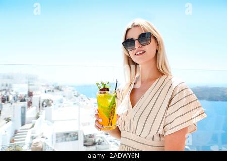 Pretty woman holding a glass of passion fruit cocktail in Santorini background Stock Photo