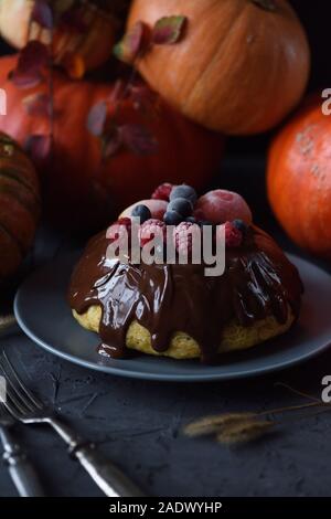 Thanksgiving hygge dessert. Homemade pumpkin pudding with chocolate icing and frozen berries and bright orange winter squashes on dark background copy Stock Photo