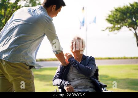 young asian adult son visiting father in nursing home giving dad a pat on the shoulder Stock Photo