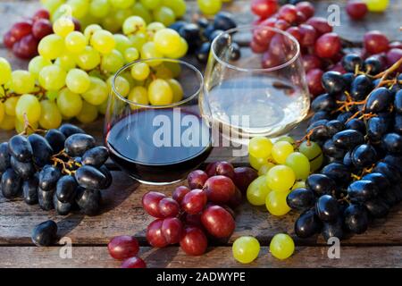 Glass of red and white wine with fresh grape assortment on wooden table. Close up Stock Photo