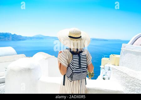 Young woman in a white dress and straw hat, walking at the city of Oia, island of Santorini, Greece. Concept of leisure, tourism, travel, vacations, r Stock Photo