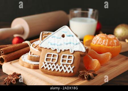 Board of homemade Christmas cookies, glass of milk, mandarin, cinnamon, candies, rocking chair on wooden background, closeup Stock Photo