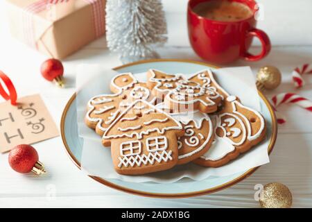 Plate with Christmas cookies, toys, gift boxes and coffee on white wooden background, closeup Stock Photo