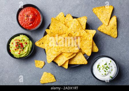 Nachos chips in bowl with sauces, dip variety. Grey stone background. Top view Stock Photo