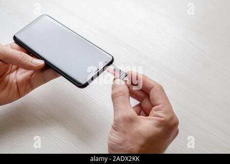 Inserting SIM and mini SD adapter into the phone concept. Hand holding adapter and inserts it into the phone. Stock Photo