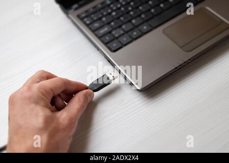 Hand holding usb cable and plugs it into the usb port on the laptop computer close-up Stock Photo