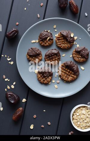 Raw vegan gluten free cookies with chocolate glaze served with ingredients: oats, dates and himalayan salt on grey plate top view Stock Photo