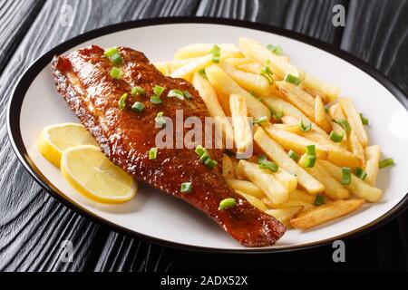Baked sea perch fish with french fries and lemon juice close-up in a plate on the table. horizontal Stock Photo
