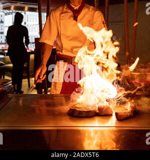 Cooking of beef teppanyaki recipe japanese grilled beef tomahawk steak on cooking pan using scraper with flame in background Stock Photo