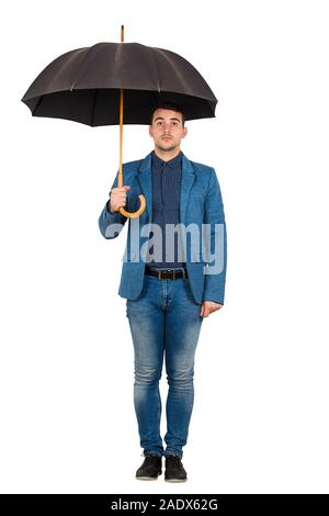Full length portrait of businessman wearing casual blue suit standing under open umbrella looking perplexed to camera isolated over white background.