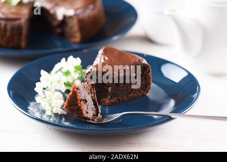 Healthy chocolate dessert. Bird cherry cake with chocolate ganache served with bird cherry flowers on dark blue plate on white background closeup Stock Photo
