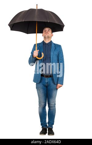 Full length portrait of confused businessman standing under open umbrella looking up perplexed isolated over white background.