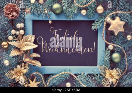 Text 'Frohliche Weihnachten' in German means 'Happy Christmas'. Green and golden Christmas background. Decorated fir twigs around chalk board on dark Stock Photo