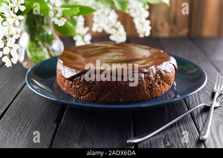 Homemade chocolate cake with chocolate icing in navy blue plate on black background served with white bird cherry flowers closeup Stock Photo