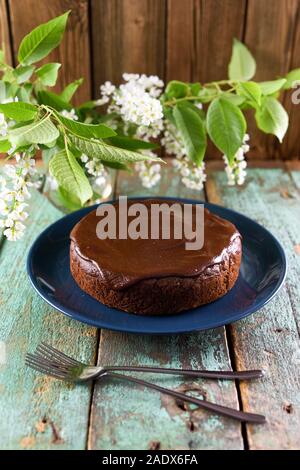 Homemade chocolate cake with chocolate icing in navy blue plate on old painted wood background served with white bird cherry flowers and two forks in Stock Photo