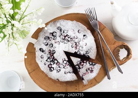 Traditional Siberian cake with bird cherries, cowberries and black currants served with white teaware and lily of the valley bouquet on oak board on w Stock Photo