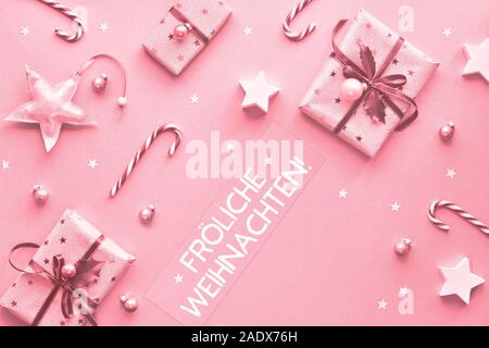 Festive monochrome pink Christmas background. Text 'Frohliche Weihnachten' means 'Happy Christmas' in German. Pink gift boxes, candy canes, trinkets a Stock Photo